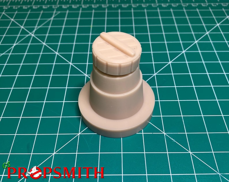 May include: A beige plastic model of a cylindrical object with a flat top and a raised, horizontal line across the top. The object is sitting on a green cutting mat.