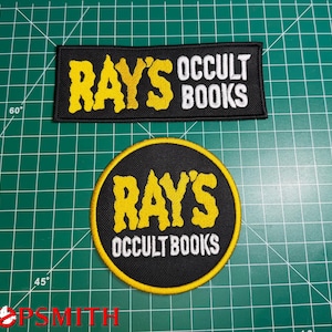 May include: Two embroidered patches with black backgrounds and yellow and white text. The rectangular patch reads RAY'S OCCULT BOOKS in yellow and white. The circular patch features a yellow border and the text RAY'S OCCULT BOOKS in yellow and white.