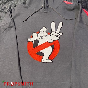 May include: A grey hooded sweatshirt with a red and white embroidered Ghostbusters logo featuring the Stay Puft Marshmallow Man giving the peace sign.