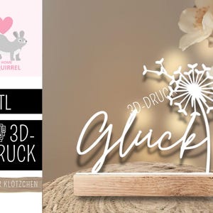 May include: A white dandelion sculpture with the word "Glück" in cursive script, mounted on a wooden base. The image also includes a squirrel graphic and text that reads ".STL", "3D-DRUCK", and "FÜR KLÖTZCHEN".