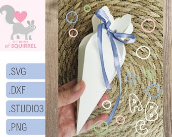 Puede incluir: Bolsa de regalo de papel blanco en forma de cono con una cinta azul. La bolsa se sostiene en una mano contra un fondo tejido con círculos de colores y las letras A, B y C.