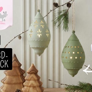 May include: Two sage green, teardrop-shaped hanging ornaments with intricate cutouts. One features a floral pattern, the other a star pattern. Both are suspended by twine. A small white LED tea light is shown to the side with an arrow pointing to the ornaments.