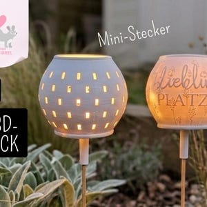 May include: Two spherical, white garden lights with a perforated design, emitting a warm glow. One light has the text "Liebling Platz". The lights are mounted on stakes, suitable for outdoor decoration. The image also includes text that says ".STL" and "3D-DRUCK".
