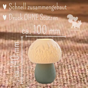 May include: A mushroom-shaped lamp with a white, textured cap featuring embossed wheat stalks and a ribbed, sage green base. The lamp measures approximately 100 mm in width and 140 mm in height. Text on the image reads: Schnell zusammengebaut, Druck OHNE St&uuml;tzen, ca. 100 mm, ca. 140 mm.