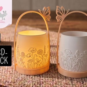 May include: Two candle holders with floral patterns. One is illuminated, revealing the etched flowers, the other is not. Both have a handle with a butterfly detail. The base and handle are a pale peach colour.