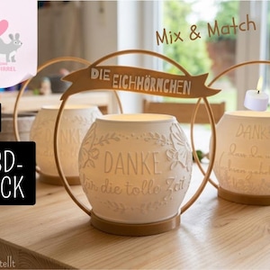 May include: Three white spherical candle holders with embossed floral patterns and German text. Each holder sits in a gold-coloured circular frame with a banner at the top reading DIE EICHHÖRNCHEN. The text on the front reads DANKE für die tolle Zeit.