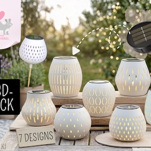 May include: A collection of white solar-powered lanterns with various cut-out designs. The lanterns are arranged on a wooden surface, with a blurred outdoor background. The image also includes a solar panel and a small candle.