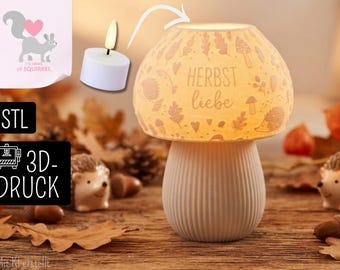 Könnte beinhalten: Eine pilzförmige Lampe mit geripptem Fuß und einem Schirm, der mit herbstlichen Motiven wie Igeln, Blättern und Pilzen sowie dem Schriftzug "HERBST liebe" graviert ist, beleuchtet durch ein kleines, weißes Teelicht im Inneren des Schirms.