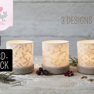 May include: Three cylindrical candle holders with illuminated white shades featuring embossed patterns of holly leaves, pine branches, and snowflakes. Each holder has a textured, knit-look base. Text includes 3 DESIGNS, .STL, and 3D-DRUCK.