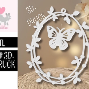Puede incluir: Una corona floral y de mariposa blanca impresa en 3D. La mariposa está suspendida dentro del marco ovalado de la corona. La corona está decorada con hojas y pequeños puntos. La imagen también incluye el texto "3D-DRUCK".