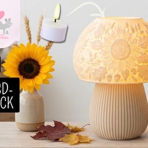 May include: A mushroom-shaped lamp with a textured, off-white shade featuring embossed sunflower, leaf, and acorn patterns. The base is vertically ribbed. A small white tea light candle is shown above the lamp, indicating it is the light source.