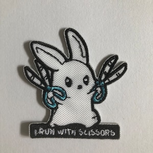 May include: White embroidered patch of a rabbit holding two pairs of blue scissors with the text "Run with Scissors" below.