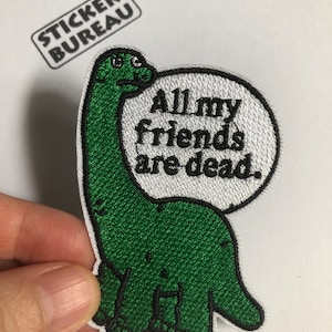 Puede incluir: Parche verde bordado de un dinosaurio con un globo de diálogo que dice "All my friends are dead."