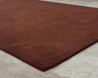 May include: A rectangular, solid brown rug. The rug is made of a soft, plush material and is placed on a concrete surface. The rug's color is a deep, rich brown, and it appears to be new.