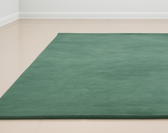Puede incluir: Una alfombra rectangular verde liso. La alfombra es de un tono verde apagado y parece estar hecha de un material suave. La alfombra está colocada sobre un suelo de baldosas de color claro. Un artículo de decoración del hogar.