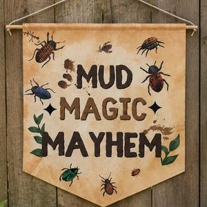 May include: A rustic outdoor mud kitchen setup with a wooden banner that reads "Mud Magic Mayhem" and a chalkboard sign that says "Play Dirty Be Happy". The scene includes gardening tools and plants.