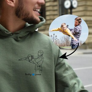 May include: A green hooded sweatshirt with a line drawing of a father and child playing, with the text "Daddy & James" underneath the drawing.