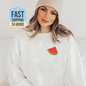May include: White sweatshirt with a watermelon graphic on the front. The watermelon is red with black seeds and a green rind.