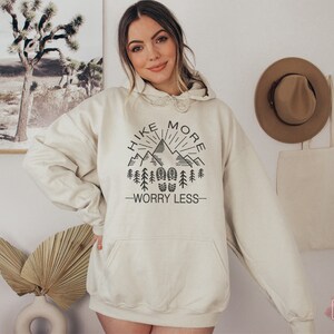 May include: A cream-colored hoodie with a black graphic that says "Hike More Worry Less" with a mountain range and trees.