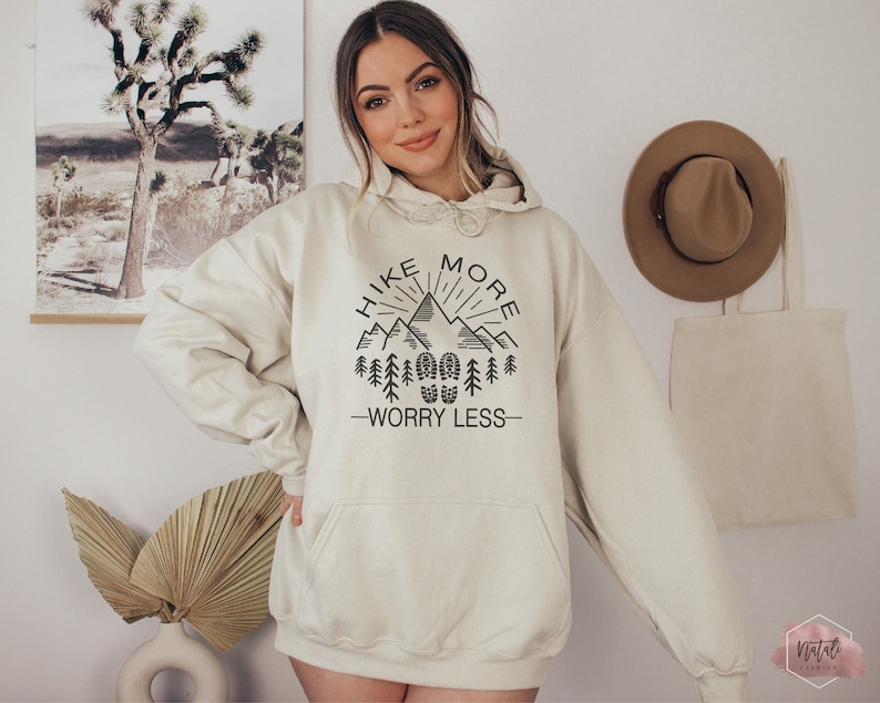 May include: A cream-colored hoodie with a black graphic that says "Hike More Worry Less" with a mountain range and trees.