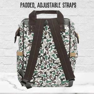 The back side of our camouflage-patterned backpack with padded, adjustable straps. The backpack is primarily green, white, and brown, with a dark brown canvas strap. The text 'PADDED, ADJUSTABLE STRAPS' is displayed at the top.