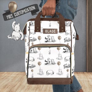 Custom Diaper Bag Backpack Winnie the Pooh Baby Bag with Personalized Name Gift for Baby. Our custom winnie the pooh diaper backpack is perfect for baby boys or girls and the perfect unisex gift for a baby shower. Our bag has pooh bear, tigger, eyore, piglet and Christopher robin as the public domain characters in the original winnie the pooh book.