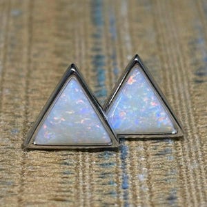May include: A pair of silver triangle stud earrings with white opal stones.