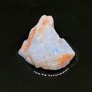 Könnte beinhalten: Ein roher, weißer Opal mit irisierenden Farbschimmern. Der Opal hat eine rotbraune Matrix.