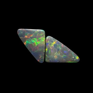 May include: Two triangular-shaped black opals featuring a dark base color with vibrant flashes of green, yellow, and red play-of-color. The gemstones have a smooth, polished surface and irregular, angular edges, displaying a distinct iridescent pattern.