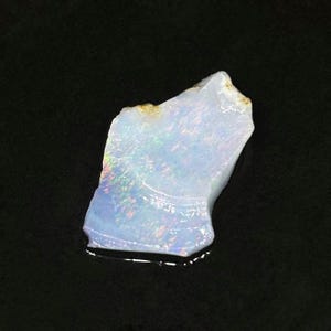 May include: A rough, white opal gemstone with iridescent flashes of color. The opal is a natural stone with a unique and beautiful pattern.