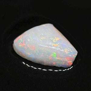 Puede incluir: Una piedra preciosa de ópalo blanco con destellos iridiscentes de color, incluyendo rojo, verde y azul.