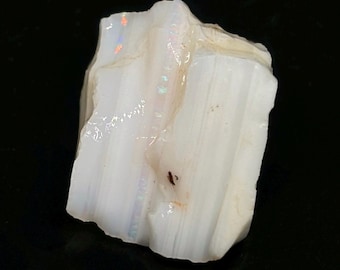 May include: A white opal rough with iridescent flashes of color. The opal is a natural stone with a rough, irregular shape.