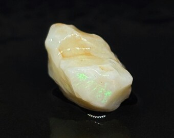 May include: A rough, white opal gemstone with green and orange flashes of colour.