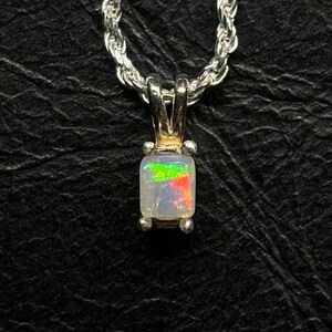 May include: A silver chain necklace with a square-shaped opal pendant. The opal is white with iridescent green, red, and yellow flashes.