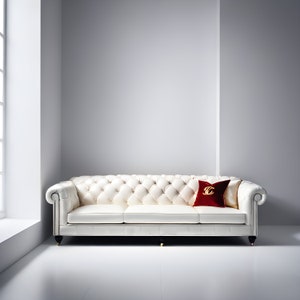May include: A white leather tufted sofa with a red pillow featuring a gold logo. The sofa has a classic design with rolled arms and wooden legs.