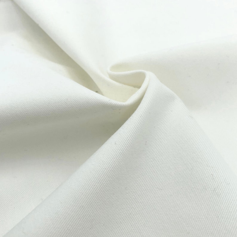 K&ouml;nnte beinhalten: Nahaufnahme eines wei&szlig;en Baumwollstoffs mit einer subtilen K&ouml;perbindung. Der Stoff ist glatt und hat eine weiche Textur.