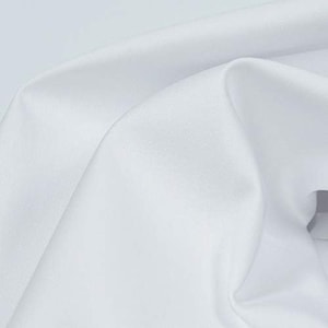 K&ouml;nnte beinhalten: Wei&szlig;er Baumwollstoff mit einer glatten, gleichm&auml;&szlig;igen Textur. Der Stoff ist gefaltet und drapiert und zeigt seine weiche und flie&szlig;ende Beschaffenheit.