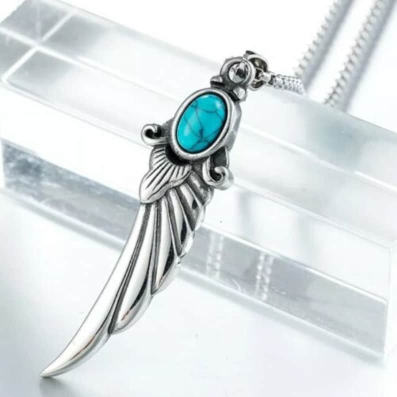 Op de afbeelding: Een zilveren ketting met een hanger in de vorm van een vleugel met een turquoise steen.
