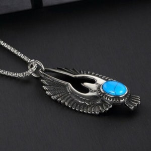 May include: A silver necklace with a pendant featuring a detailed eagle design with spread wings and a turquoise gemstone in the center.
