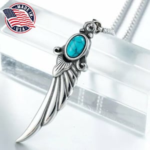 Op de afbeelding: Zilveren ketting met hanger, een turquoise steen en een vleugelontwerp. De ketting is zilverkleurig en heeft een doosgesp.