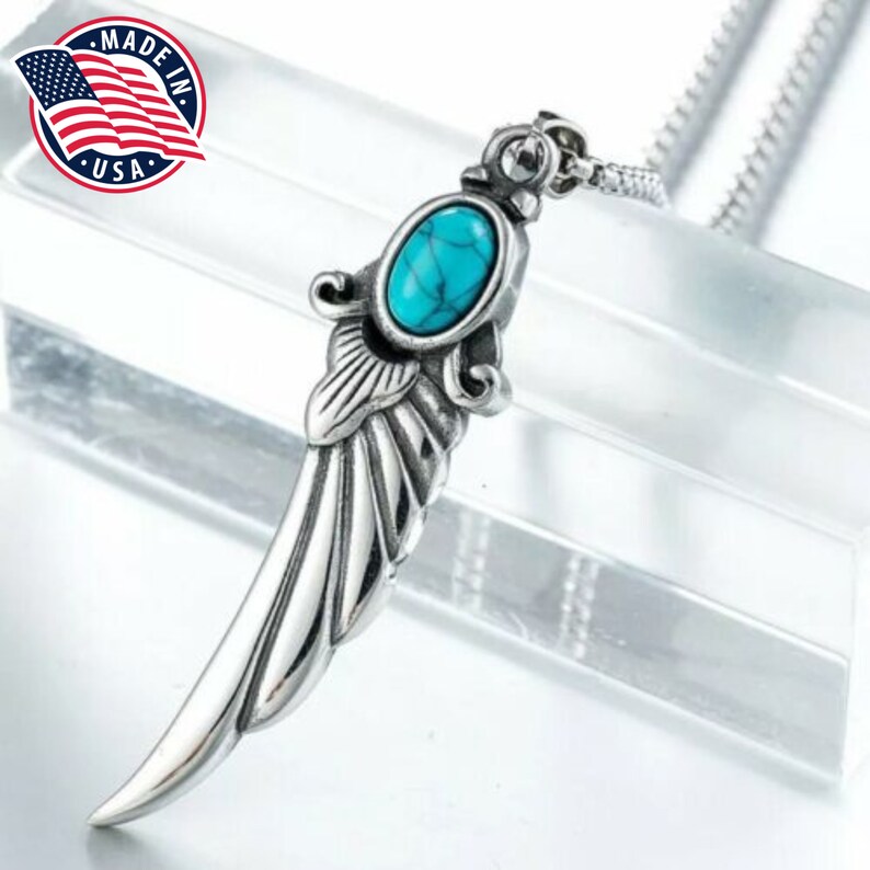 Op de afbeelding: Zilveren ketting met hanger, een turquoise steen en een vleugelontwerp. De ketting is zilverkleurig en heeft een doosgesp.