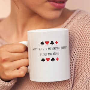 May include: White ceramic mug with black text that reads "Everything in moderation except bridge and wine".  The text is surrounded by four playing card suit symbols: a spade, a heart, a club, and a diamond.