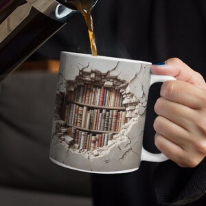 K&ouml;nnte beinhalten: Wei&szlig;e Keramiktasse mit einem einzigartigen Design, das ein B&uuml;cherregal durch eine zerbrochene Wand zeigt. Die Tasse wird mit Kaffee gef&uuml;llt. Das Design umfasst eine Vielzahl von Buchr&uuml;cken in Braun-, Rot- und Beiget&ouml;nen.