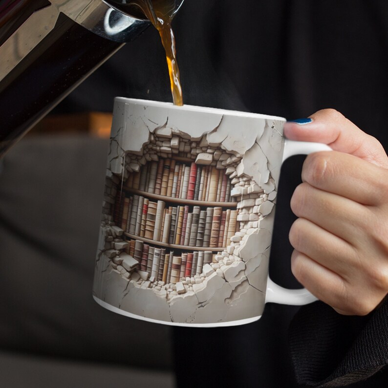 K&ouml;nnte beinhalten: Wei&szlig;e Keramiktasse mit einem einzigartigen Design, das ein B&uuml;cherregal durch eine zerbrochene Wand zeigt. Die Tasse wird mit Kaffee gef&uuml;llt. Das Design umfasst eine Vielzahl von Buchr&uuml;cken in Braun-, Rot- und Beiget&ouml;nen.