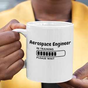 Può includere: Una tazza in ceramica bianca con una grafica nera che recita "Aerospace Engineer In Training" con una barra di avanzamento e il testo "Attendi prego".