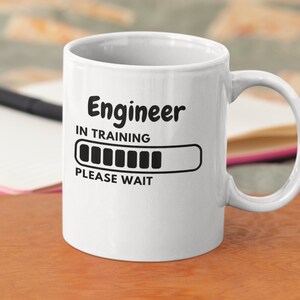 Op de afbeelding: Een witte keramische koffiemok met zwarte tekst die "Engineer in Training" zegt en een bijna volle voortgangsbalk. De tekst "Please Wait" staat onder de voortgangsbalk.