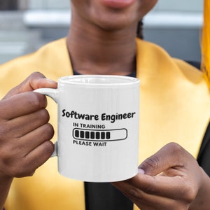 Puede incluir: Taza de café de cerámica blanca con texto negro que dice "Software Engineer In Training" y una barra de progreso que dice "Please Wait".