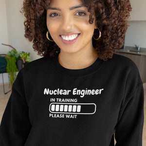 May include: Black sweatshirt with the text "Nuclear Engineer IN TRAINING PLEASE WAIT" in white. The design includes a loading bar graphic. The sweatshirt is a crew neck style.