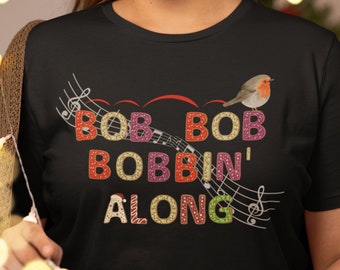 May include: Black t-shirt with a Christmas-themed design featuring the words "Bob Bob Bobbin' Along" in colourful, decorated letters. A red robin bird is perched on a musical note.