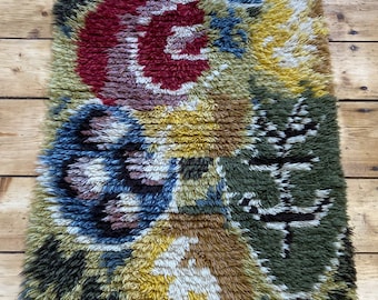 May include: A colorful, abstract rug with a floral design. The rug is made of a thick, fuzzy material and features shades of red, blue, yellow, green, and brown.